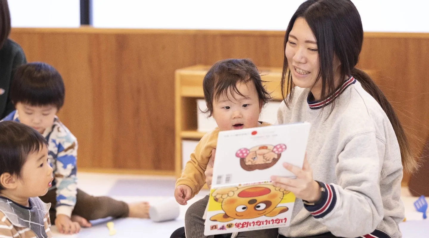 保育園の先生が子供に絵本の読み聞かせをしている画像